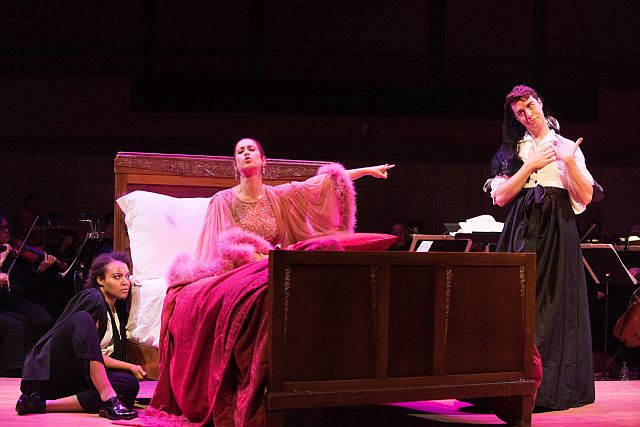 Tenor Josh Lovell (right) as Le Comte Ory in the Rossini opera scene at the Merola Schwabacher concert, with soprano Jana McIntyre as La Comtesse Adele on the bed, and mezzo Taylor Raven as Isolier. (Photo by Kristen Loken)